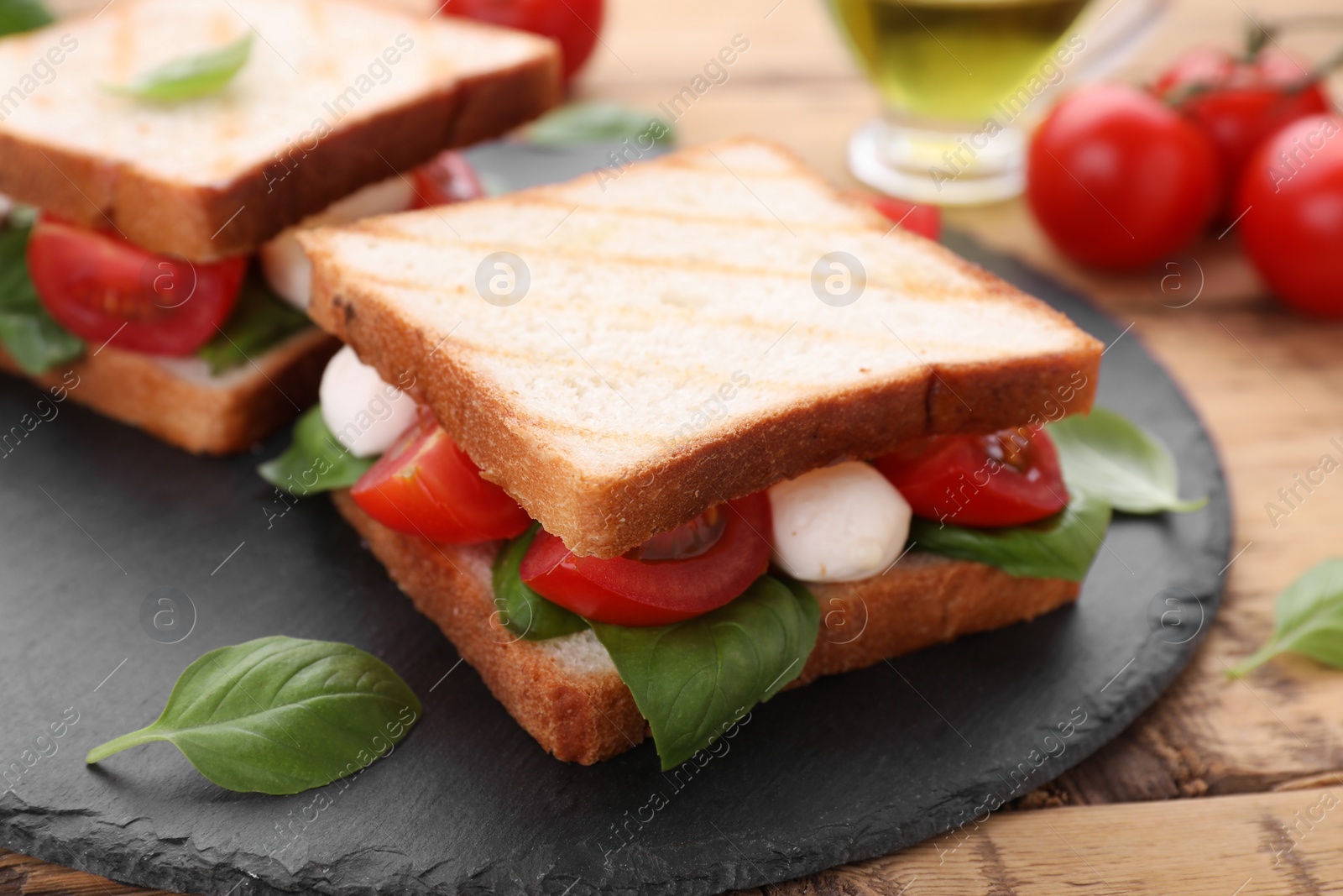 Photo of Delicious Caprese sandwiches with mozzarella, tomatoes, basil and pesto sauce on wooden table, closeup