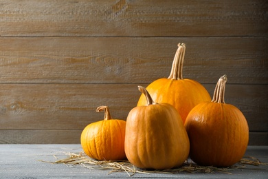 Photo of Ripe pumpkins on grey table against wooden background, space for text. Holiday decoration