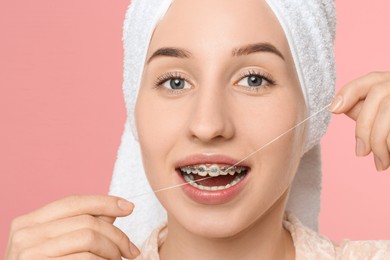 Woman with braces cleaning teeth using dental floss on pink background, closeup