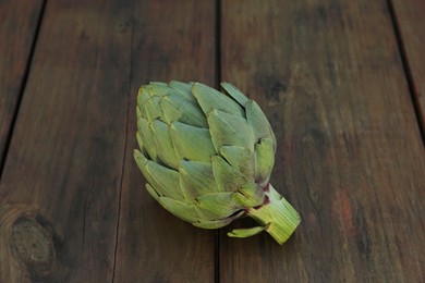 Photo of Whole fresh raw artichoke on wooden table, closeup