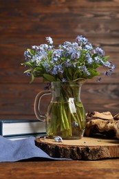 Photo of Bouquet of beautiful forget-me-not flowers in glass jug and book on wooden table