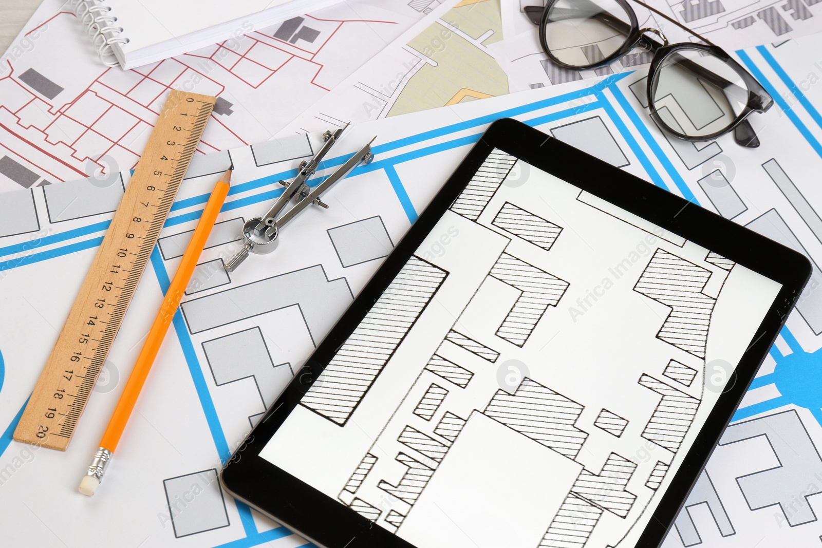 Photo of Office stationery, tablet and eyeglasses on cadastral maps of territory with buildings