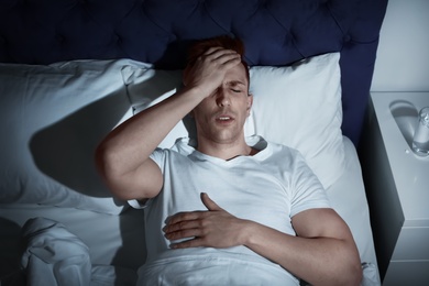 Handsome young man suffering from headache while lying in bed at night