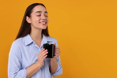 Photo of Happy young woman holding black ceramic mug on orange background, space for text