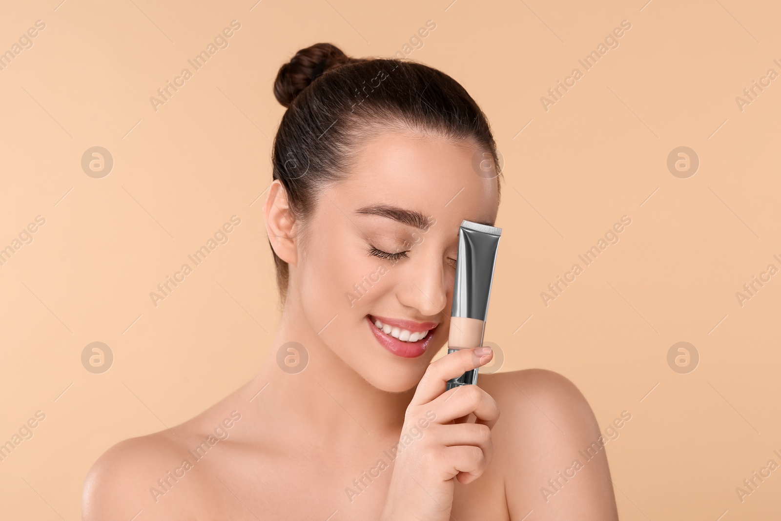 Photo of Woman holding tube of foundation on beige background