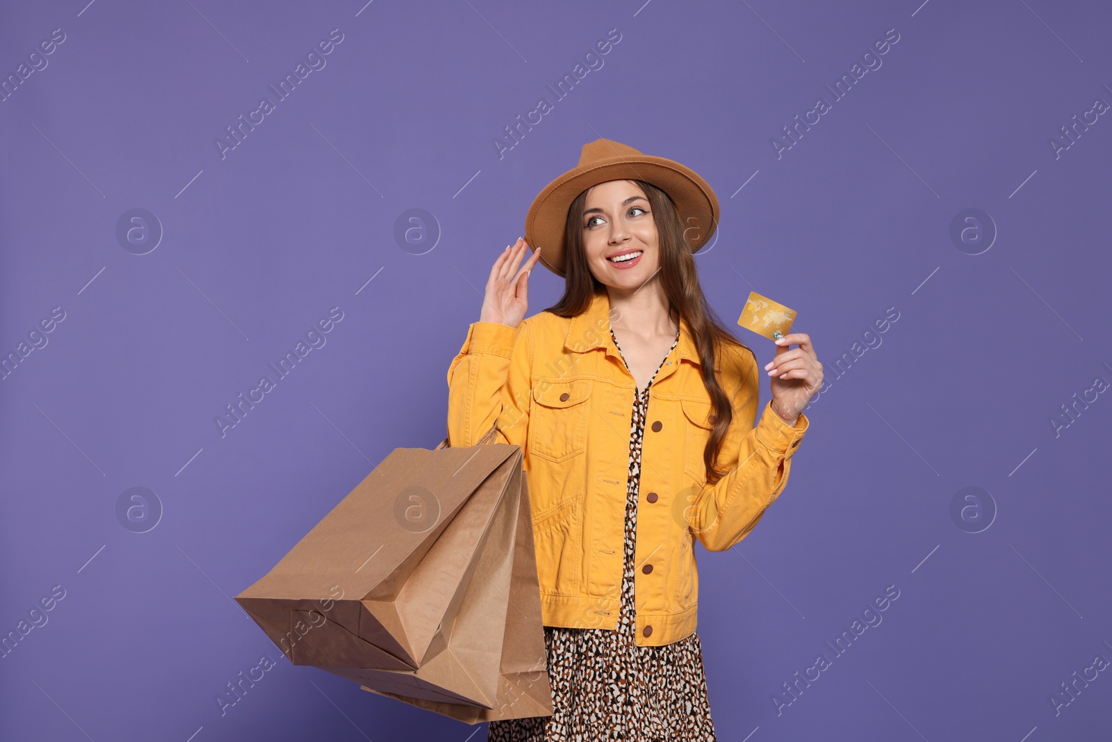 Photo of Stylish young woman with shopping bags and credit card on purple background