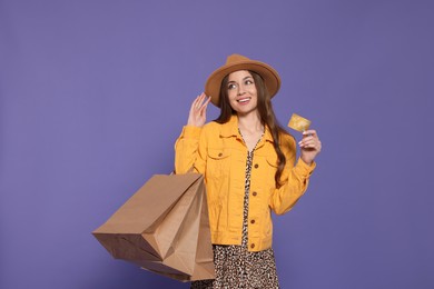 Stylish young woman with shopping bags and credit card on purple background