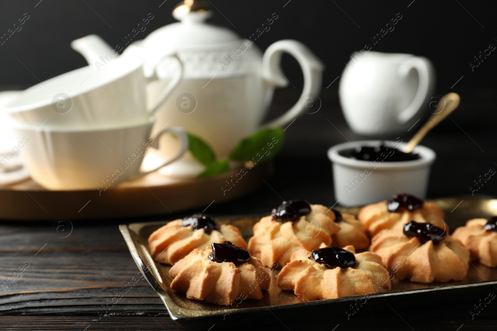 Photo of Tasty shortbread cookies with jam on black wooden table