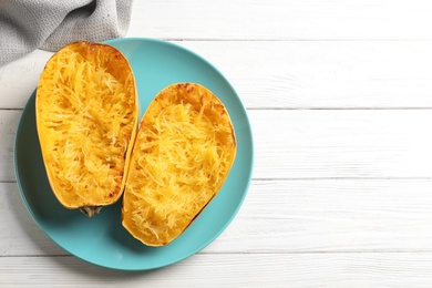 Plate with cooked spaghetti squash on white wooden background, top view. Space for text