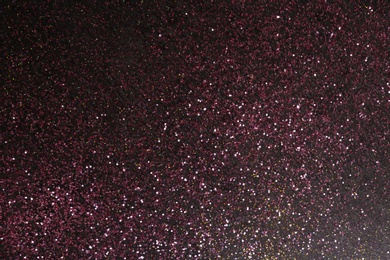 Photo of Sparkling pink glitter on dark background, top view