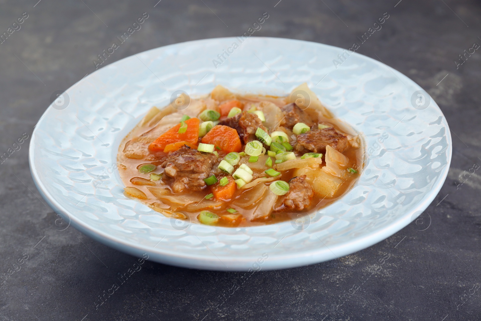 Photo of Tasty cabbage soup with meat, green onion and carrot on grey table, closeup