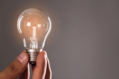 Photo of Man holding lamp bulb against gray background, closeup. Space for text