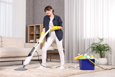 Happy young housewife vacuuming carpet at home