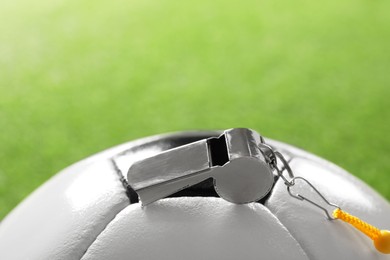 Photo of Football referee equipment. Soccer ball and metal whistle on green background, closeup with space for text