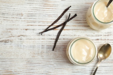 Photo of Jars with vanilla pudding and sticks on wooden background