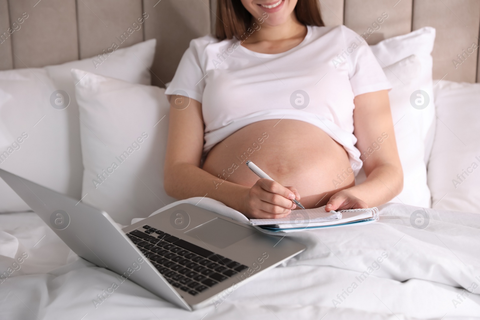 Photo of Pregnant woman working on bed at home, closeup. Maternity leave