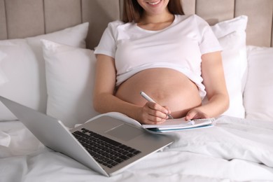 Pregnant woman working on bed at home, closeup. Maternity leave