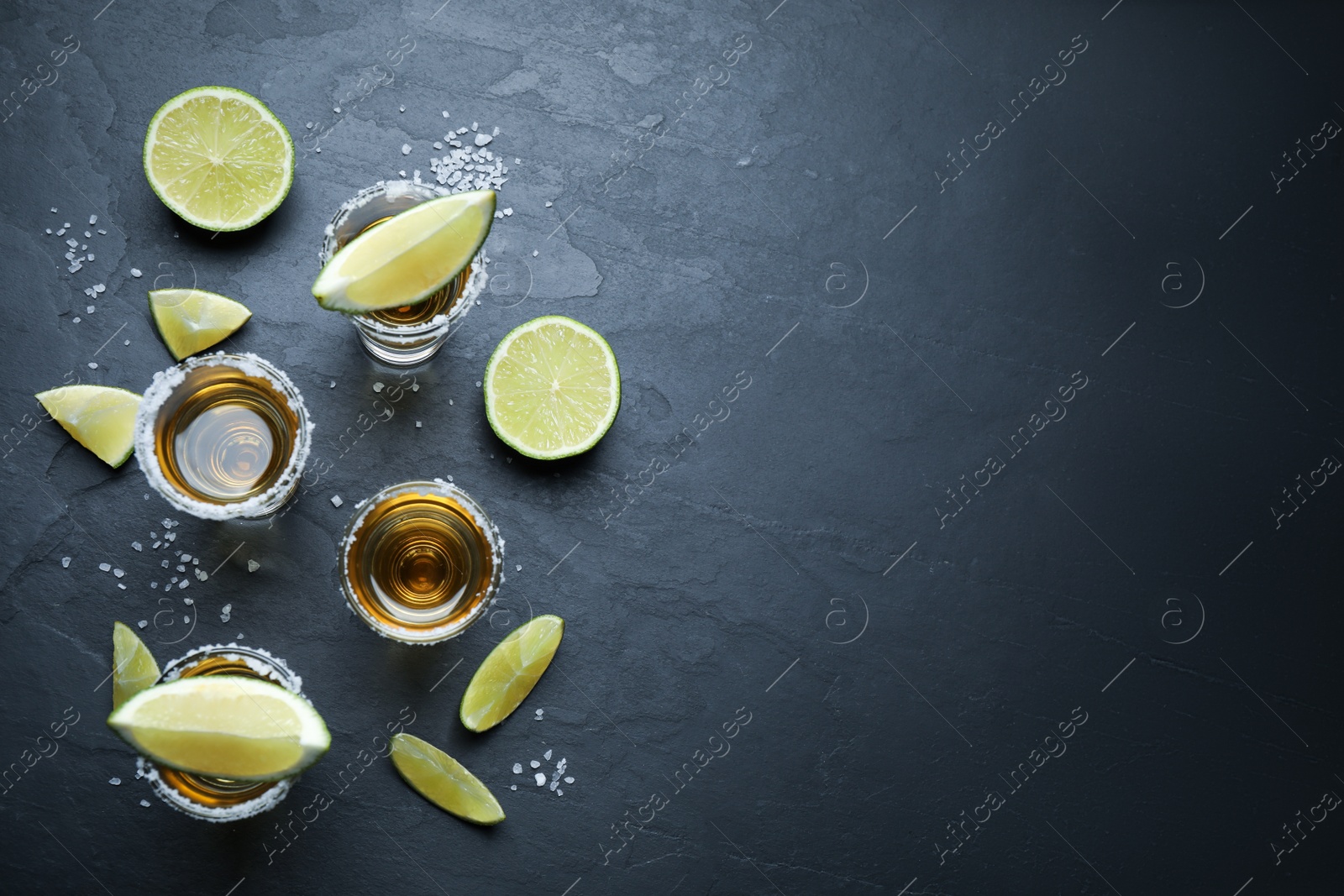 Photo of Mexican Tequila shots with salt and lime slices on grey table, flat lay. Space for text