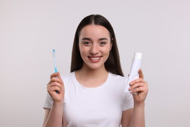 Photo of Happy woman holding plastic toothbrush and tube of toothpaste on white background