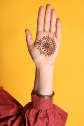 Photo of Woman with beautiful henna tattoo on hand against yellow background, closeup. Traditional mehndi