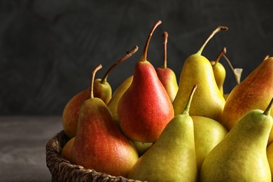 Photo of Wicker bowl with ripe pears on dark background, closeup