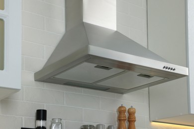 Photo of Modern range hood over shelf with spices in kitchen
