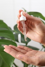 Photo of Woman applying cosmetic serum onto her hand near green plant on white background, closeup