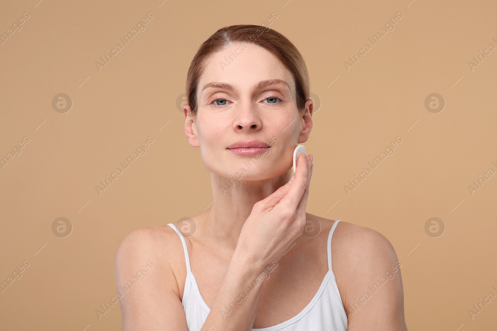 Photo of Beautiful woman removing makeup with cotton pad on beige background