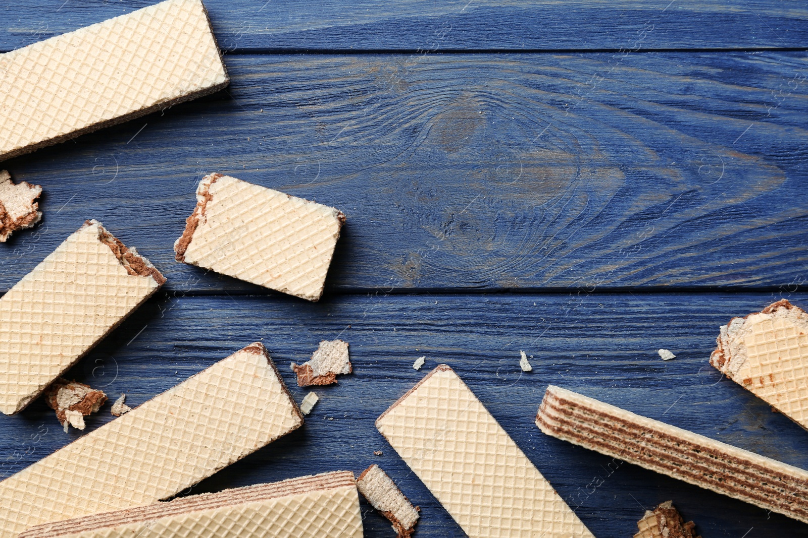 Photo of Delicious crispy wafers with chocolate filling on blue wooden table, flat lay. Space for text