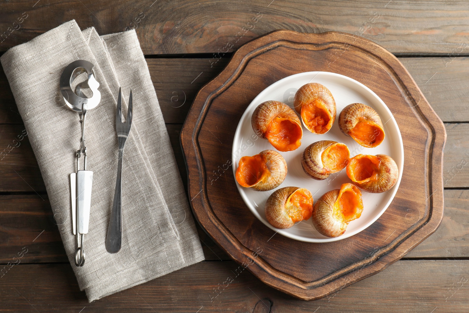 Photo of Delicious cooked snails served on wooden table, flat lay