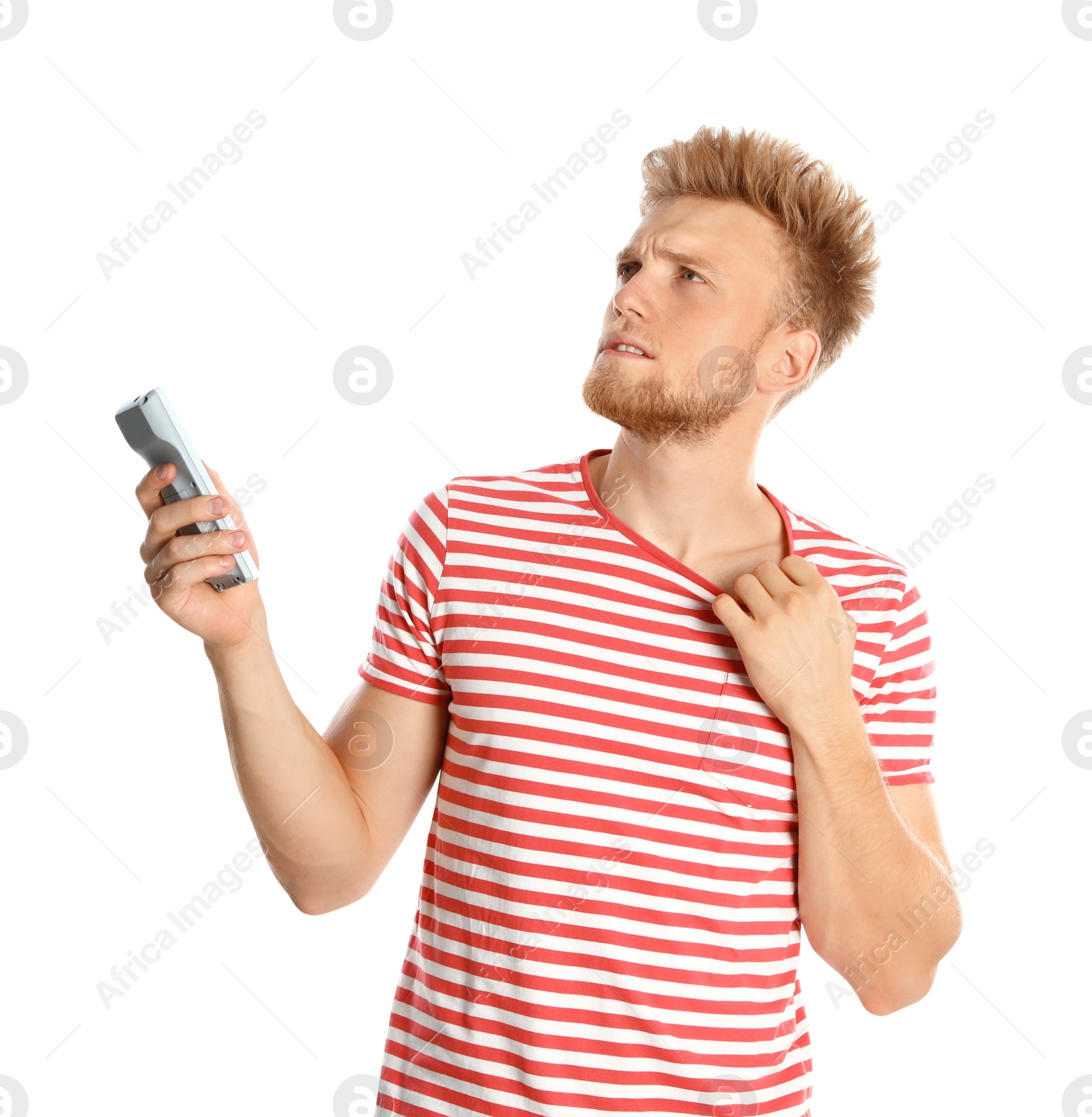 Photo of Young man with air conditioner remote suffering from heat on white background