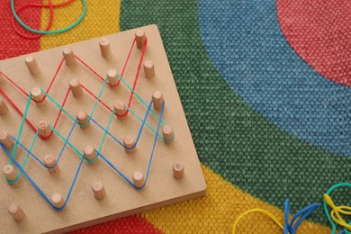 Photo of Wooden geoboard with rubber bands on carpet, space for text. Motor skills development