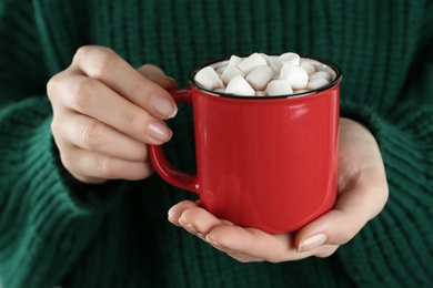 Photo of Woman in sweater holding cup of hot drink with marshmallows, closeup