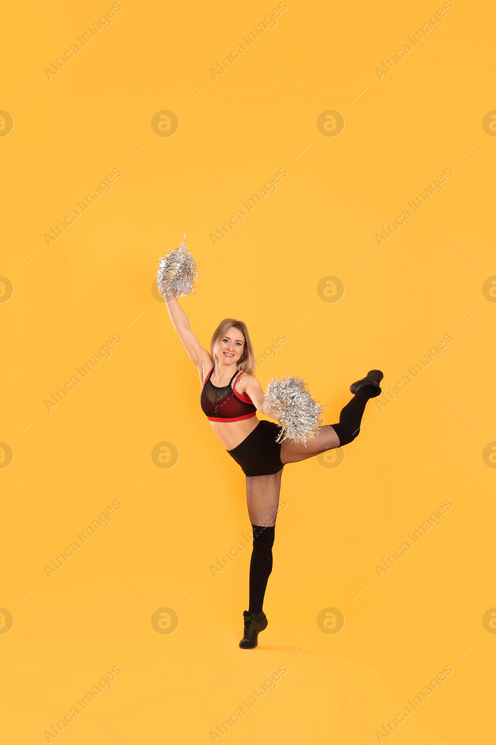 Photo of Beautiful cheerleader in costume holding pom poms on yellow background