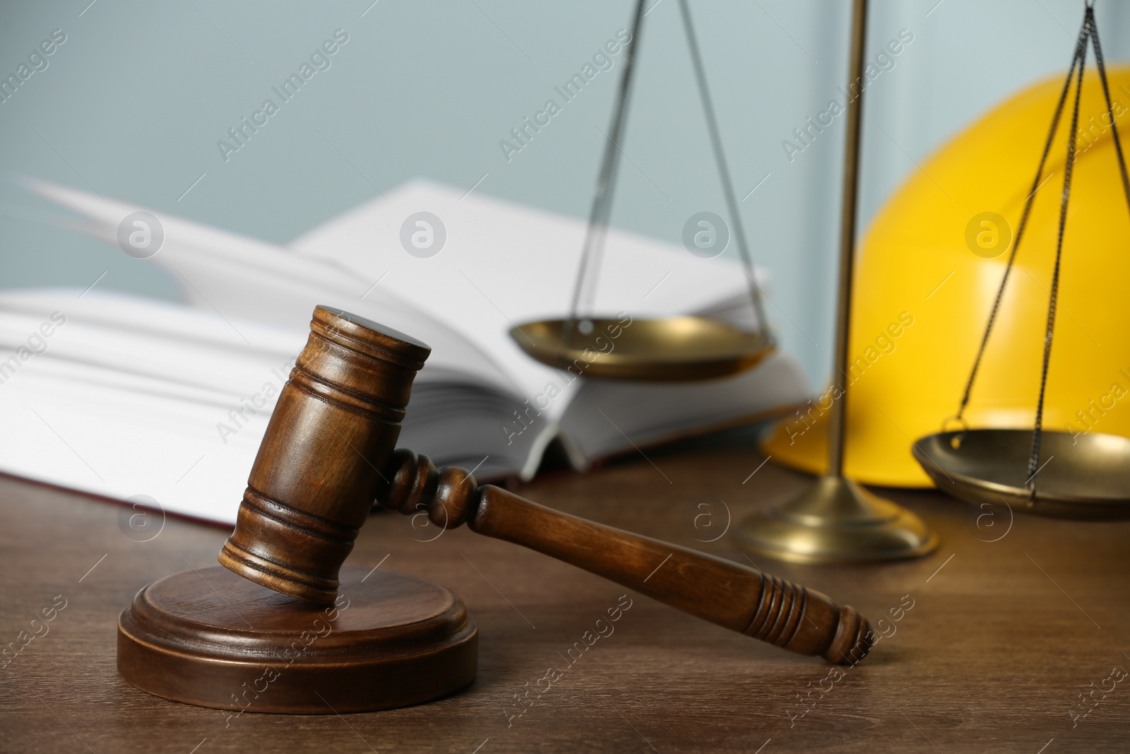 Photo of Labour, construction and land law concepts. Judge gavel, scales of justice, open book with protective helmet on wooden table