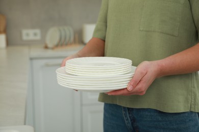 Photo of Woman holding clean plates in kitchen, closeup