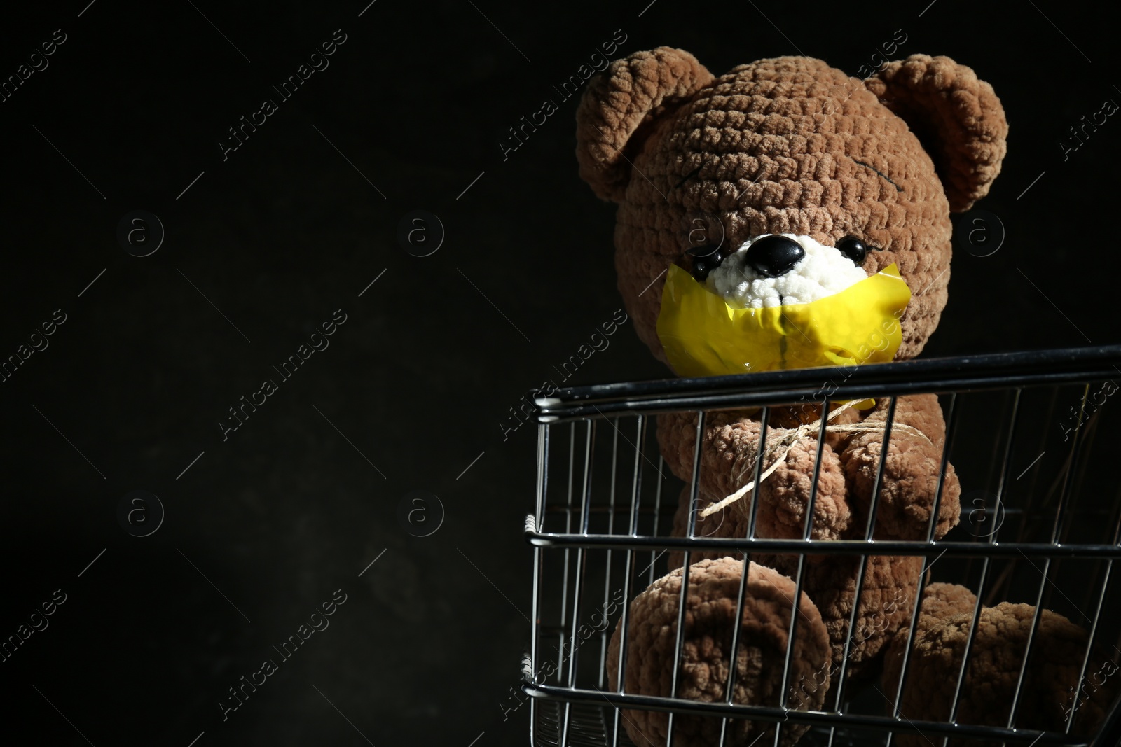 Photo of Stop child abuse. Toy bear with taped mouth on black background, closeup. Space for text