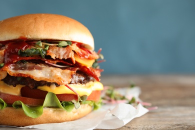 Photo of Tasty burger with bacon on table against color background, closeup. Space for text