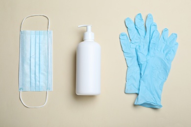 Medical gloves, mask and hand sanitizer on beige background, flat lay