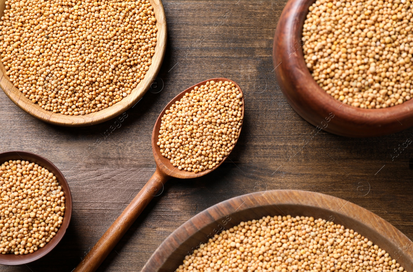 Photo of Mustard seeds in dishware on wooden table, flat lay