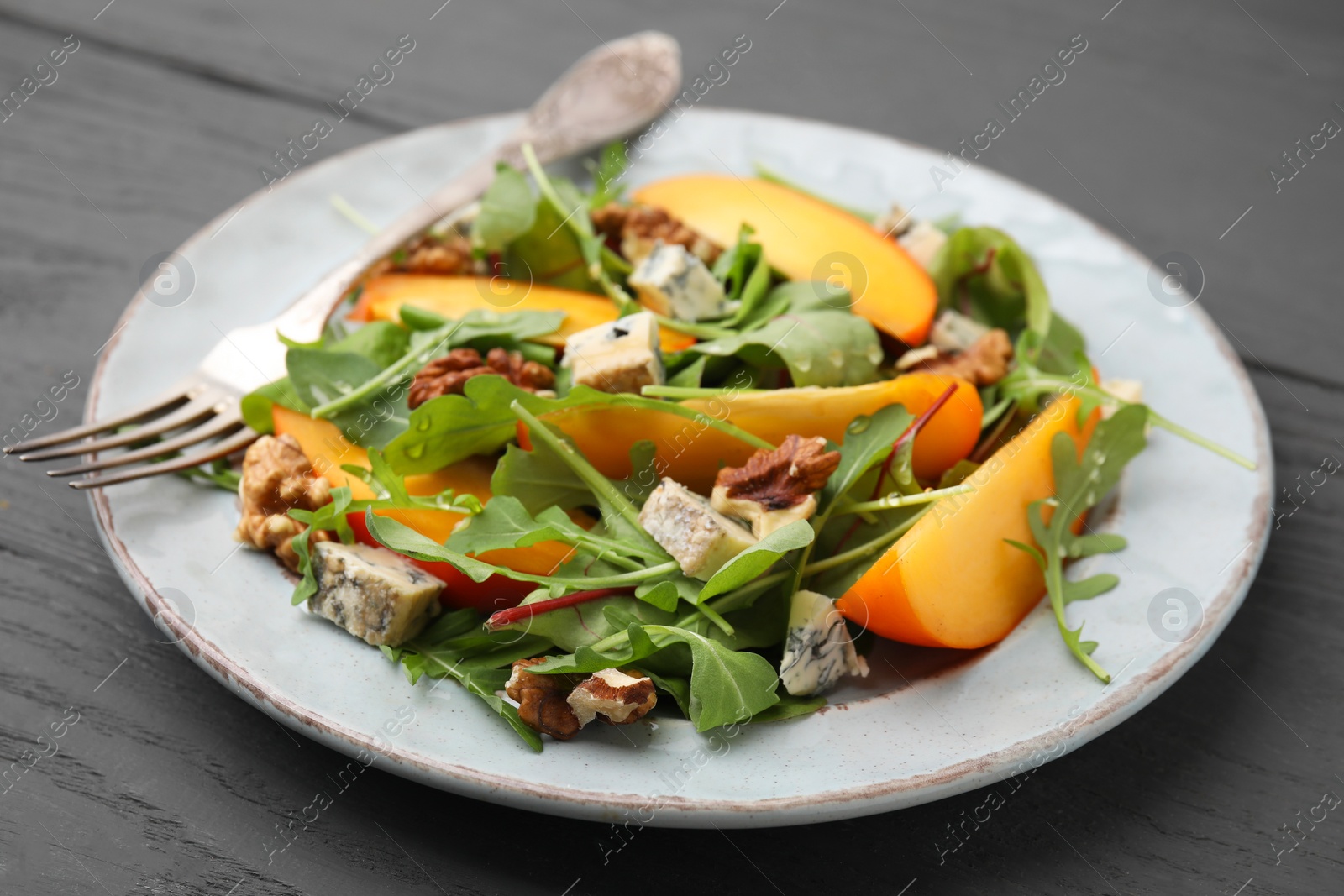 Photo of Tasty salad with persimmon, blue cheese and walnuts served on grey wooden table, closeup