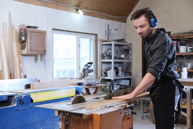 Photo of Young working man using circular saw at carpentry shop