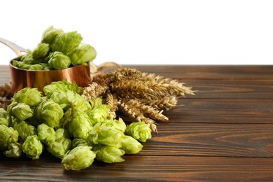Photo of Fresh hop flowers and wheat ears on wooden table against white background, space for text