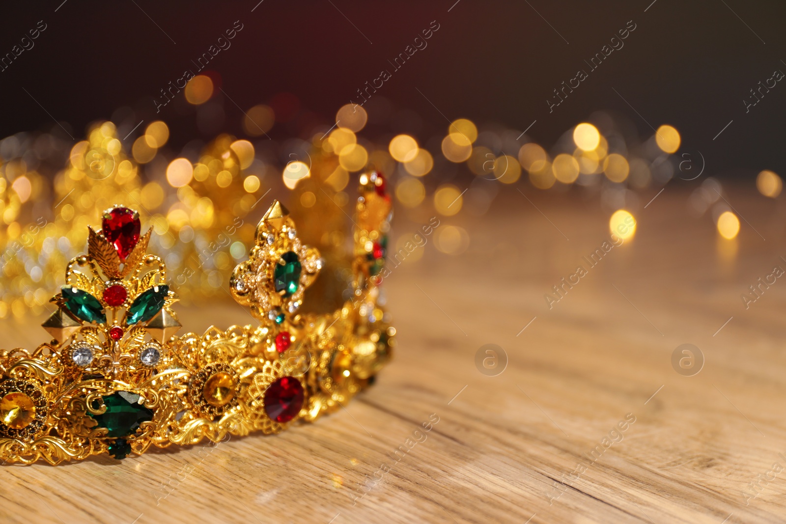 Photo of Beautiful golden crown with gems and fairy lights on wooden table, space for text. Fantasy item