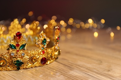 Beautiful golden crown with gems and fairy lights on wooden table, space for text. Fantasy item