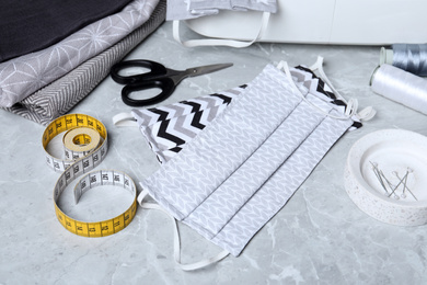 Photo of Homemade protective masks and sewing accessories on grey marble table