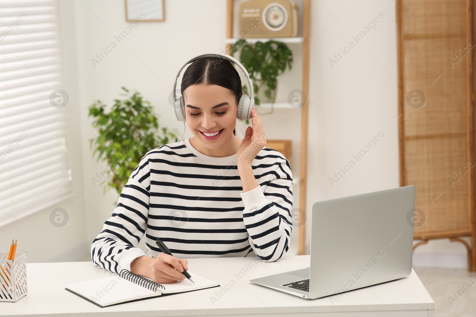 Photo of Online translation course. Student in headphones writing near laptop at home