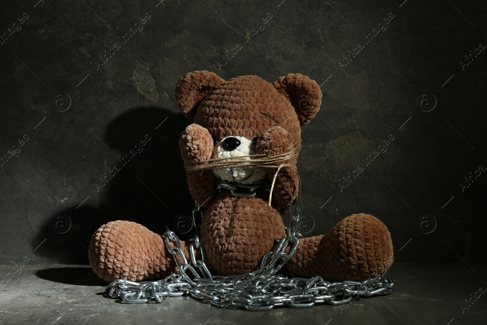 Photo of Stop child abuse. Chained toy bear covering eyes on dark grey background