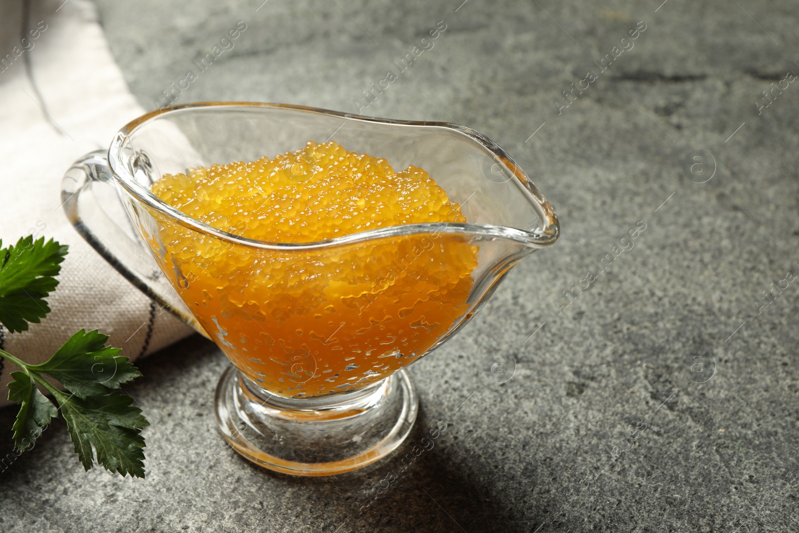 Photo of Fresh pike caviar in gravy boat and parsley on grey table, closeup