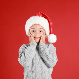 Photo of Cute little child wearing Santa hat on red background. Christmas holiday
